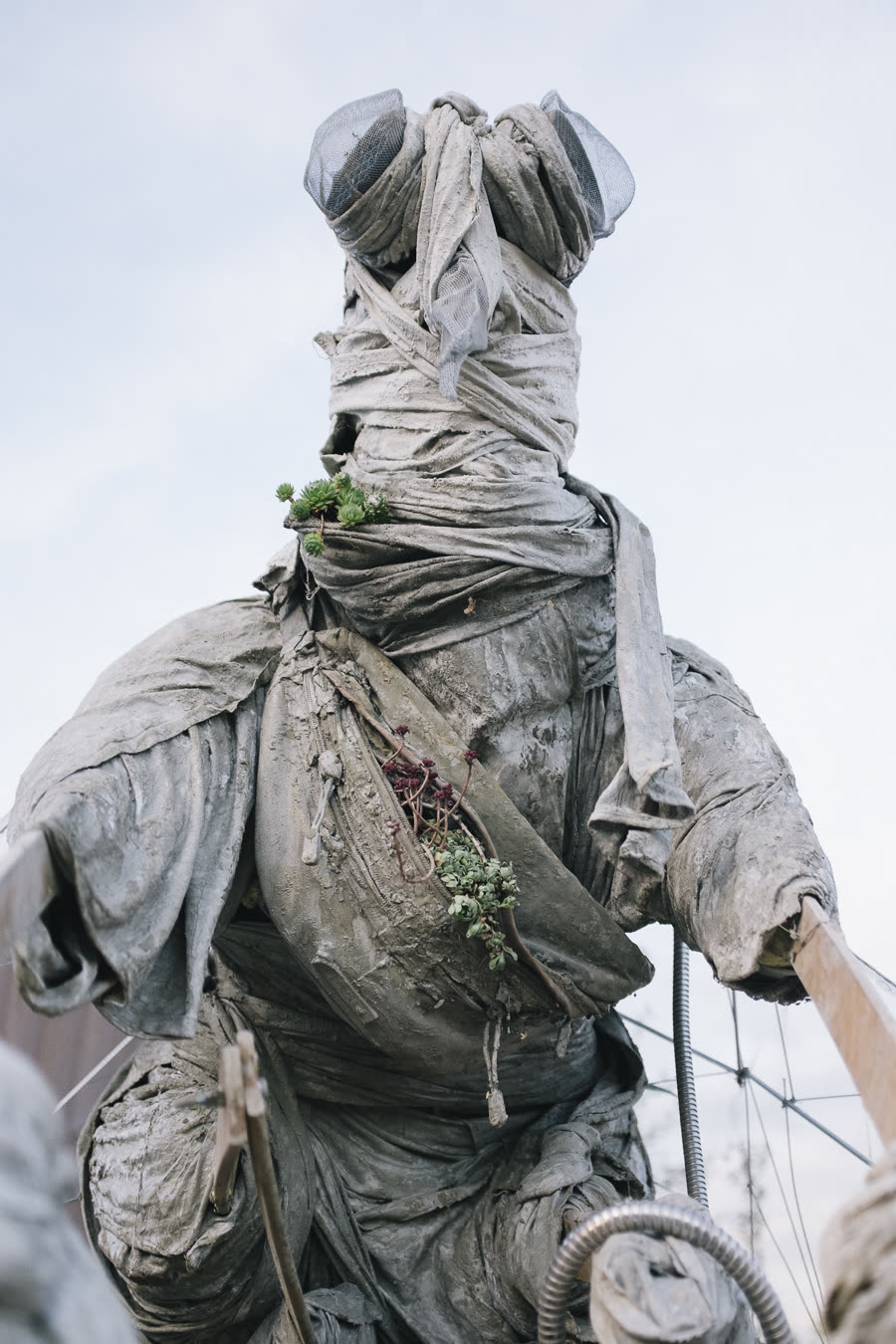 Figur von unten gegen den Himmel, mit Sukkulenten bewachsen