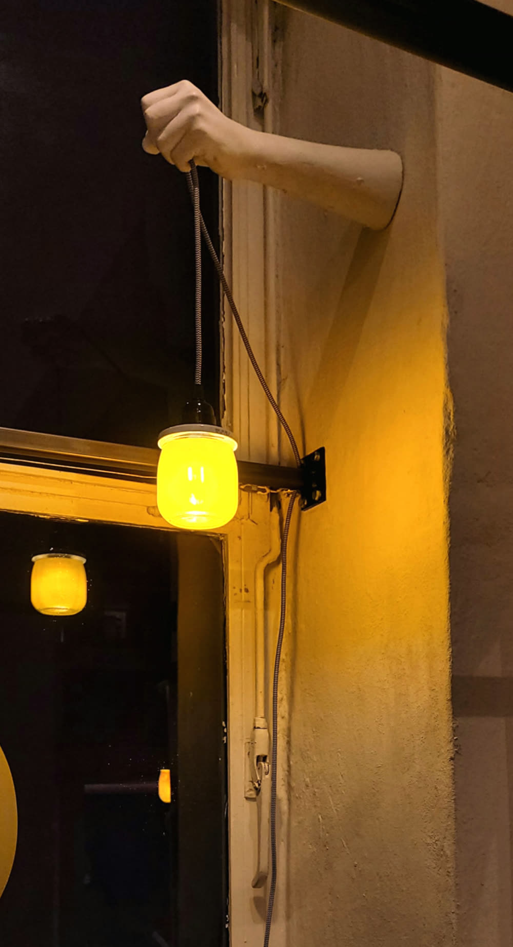 Einzelne Porzellanhand hält eine Lampe an einem Fensterrahmen, bei Nacht