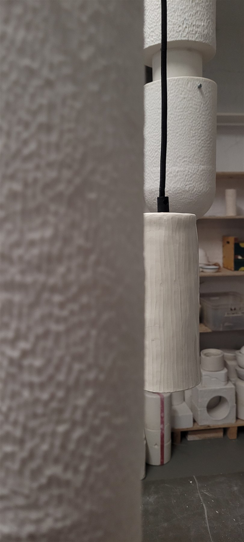 Blick in die Werkstatt: eine aufgehängte Lampe vor einem Regal mit weiteren Werkstücken