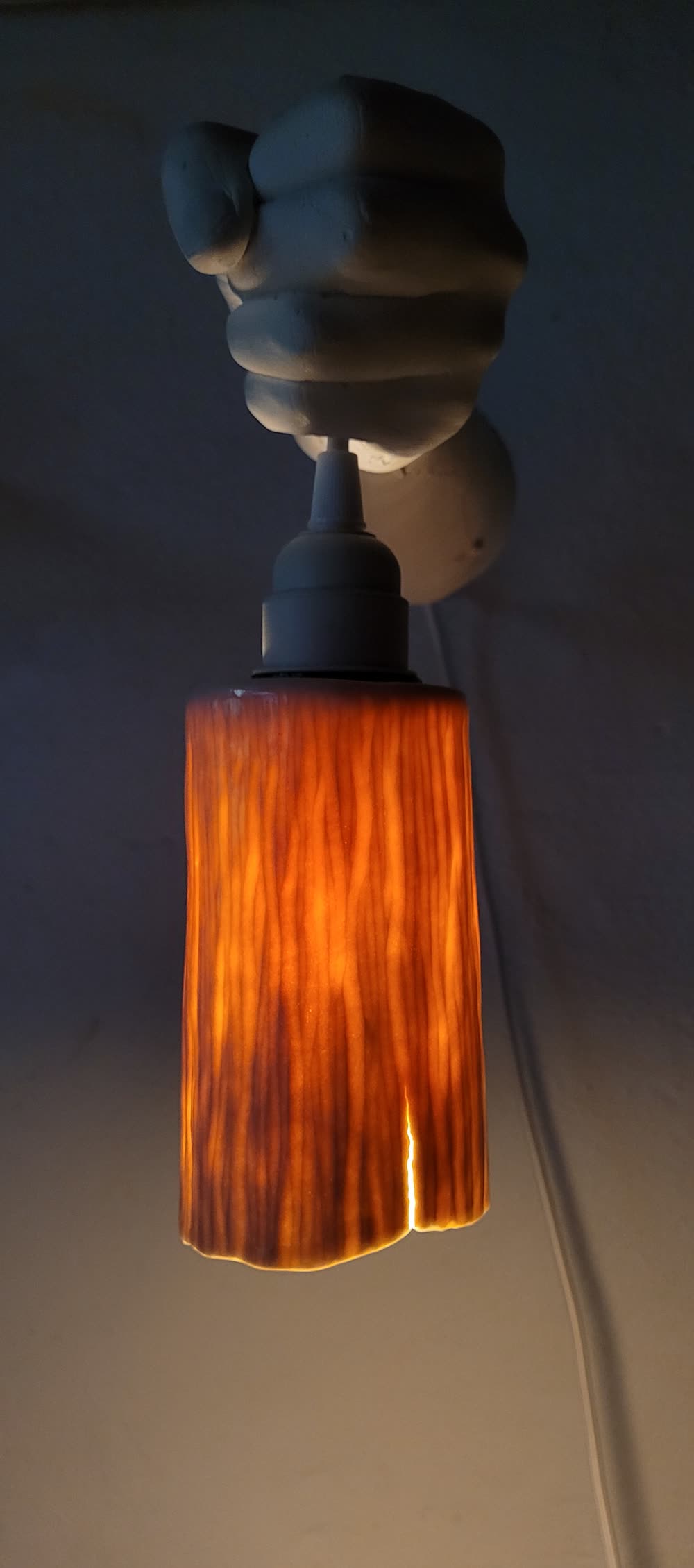 Porzellanfaust hält die Riffel-Lampe, warmes Licht von unten