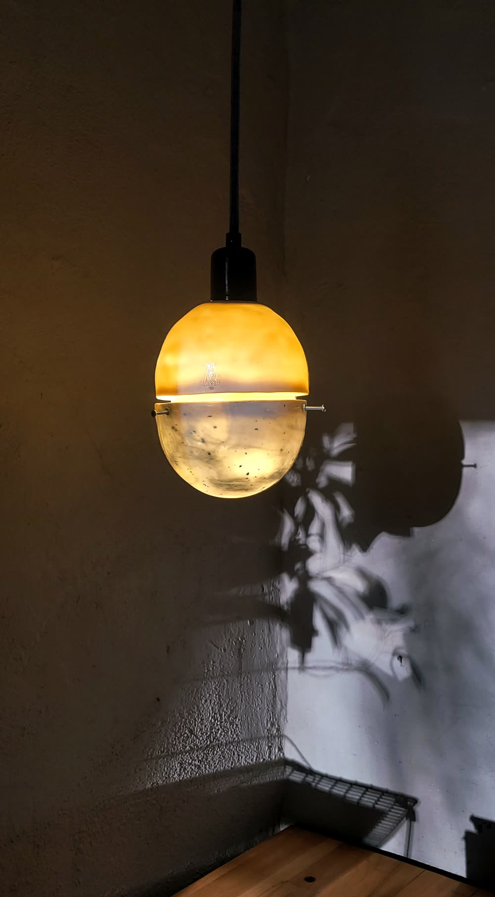 Panta-Lampe vor grauer Wand mit Pflanzenschatten